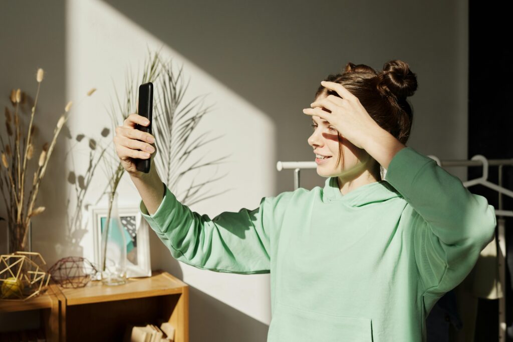 A young girl in a green hoodie takes a selfie indoors, enjoying the sunlight. Content Creation Agency