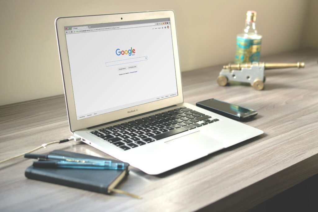 A neat workspace featuring a laptop displaying Google search, a smartphone, and a notebook on a wooden desk. SEO Services
