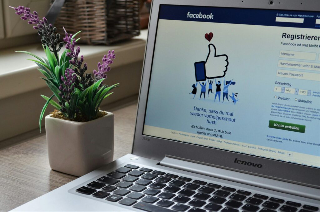 A Lenovo laptop displaying Facebook login beside a lavender plant indoors. Meta